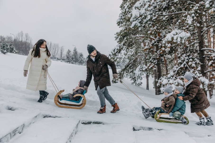Eine Familie genießt einen Spaziergang durch verschneiten Wald im Winterurlaub und zieht einen Schlitten mit. © Shutterstock