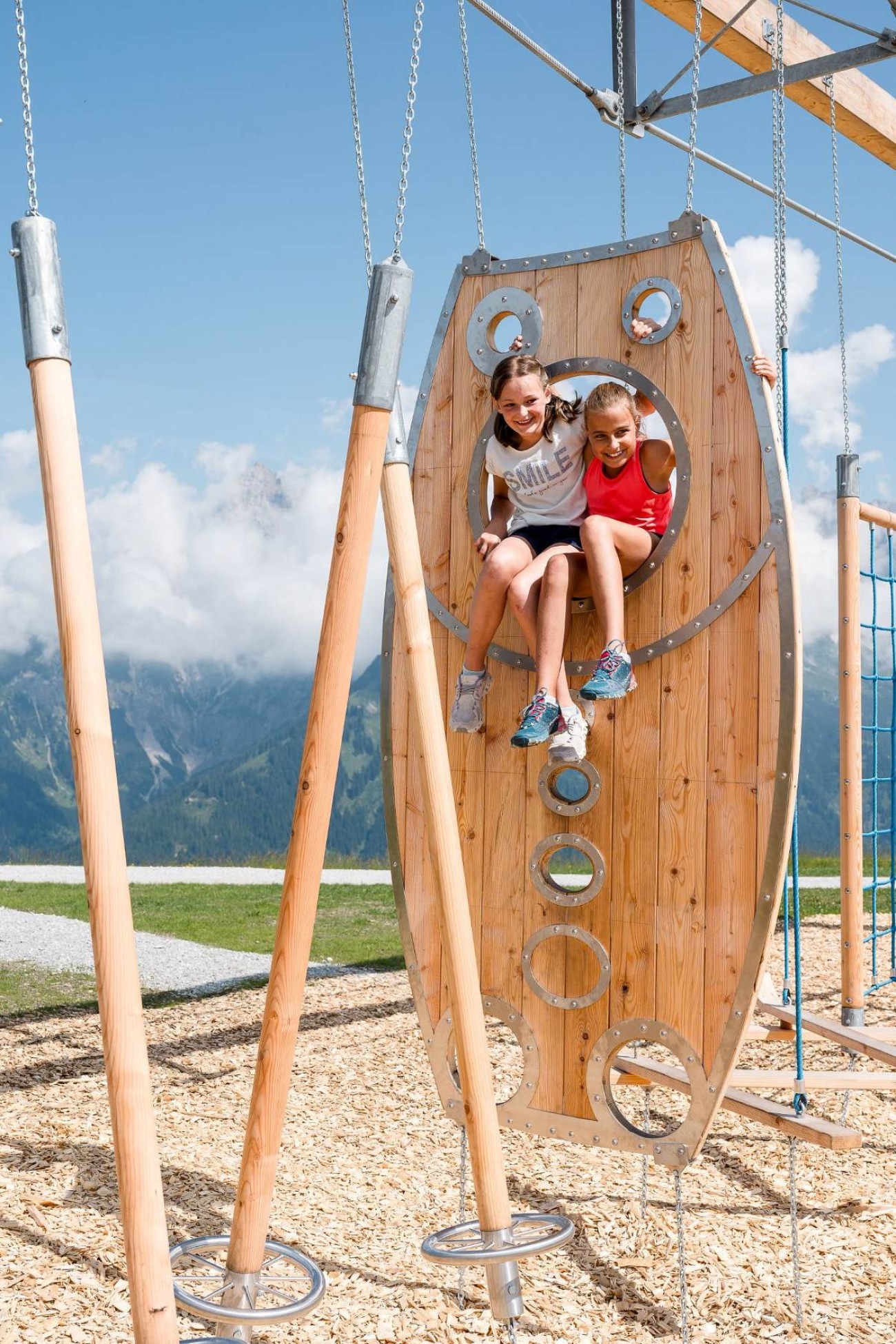 Zwei Kinder klettern auf einem hölzernen Klettergerüst im Freien mit Bergkulisse. ©TVB_Hochkönig