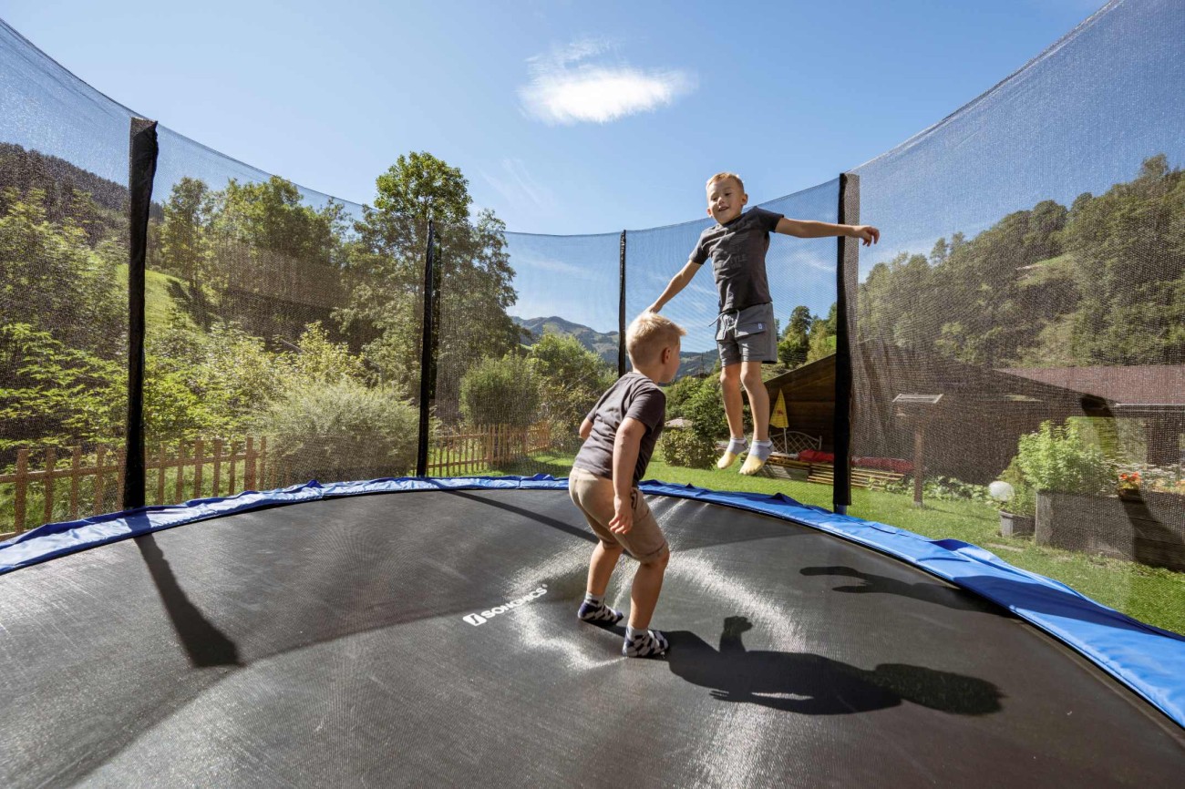 Zwei Kinder springen auf einem Trampolin im Garten an einem sonnigen Tag